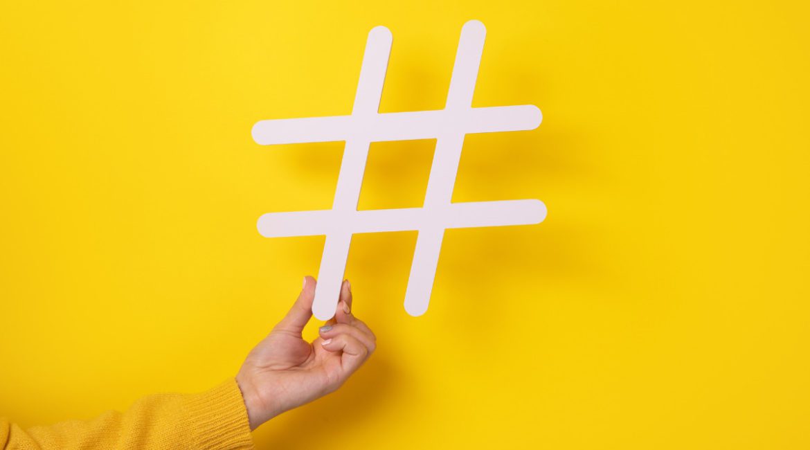 White Real Estate Hashtags Held by A Hand on a Yellow Background
