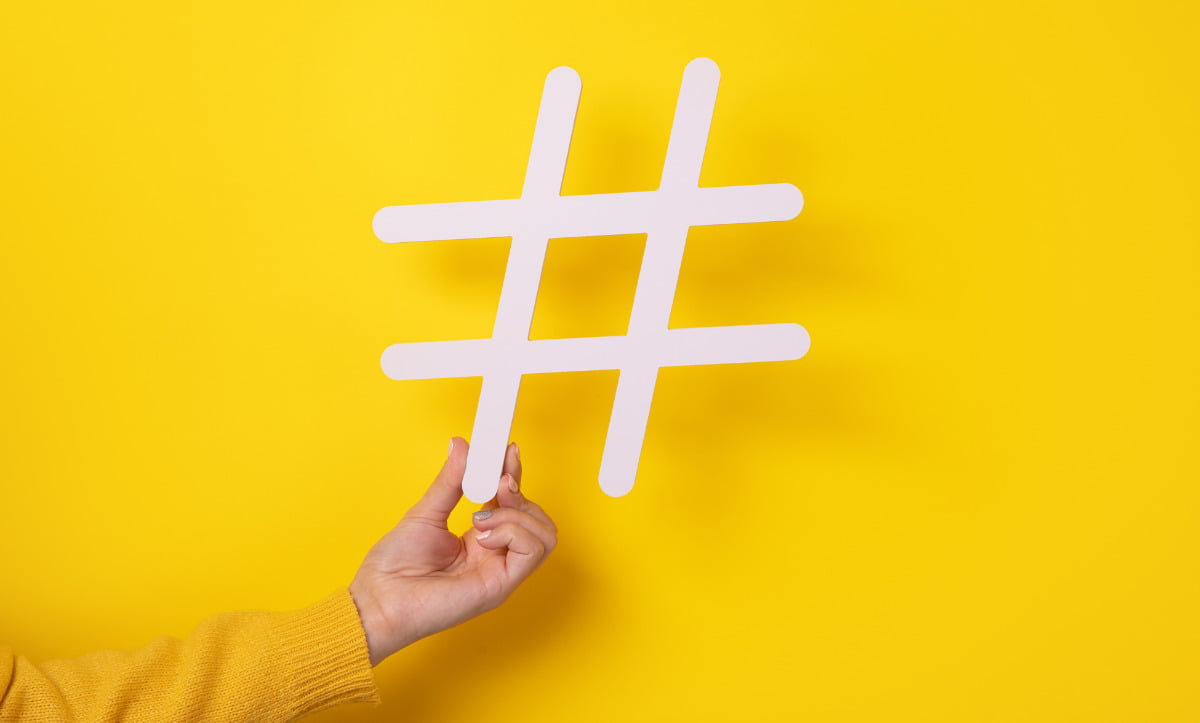 White Real Estate Hashtags Held by A Hand on a Yellow Background